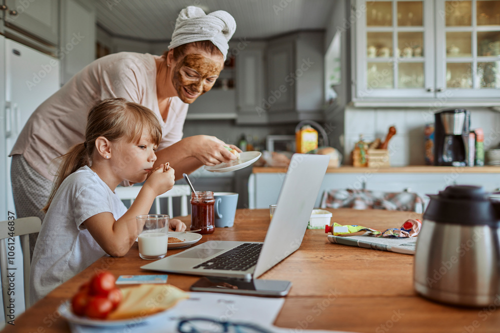 Mother and daughter having breakfast and watching laptop together in cozy kitchen Mother and daughter having breakfast and watching laptop together in cozy kitchen