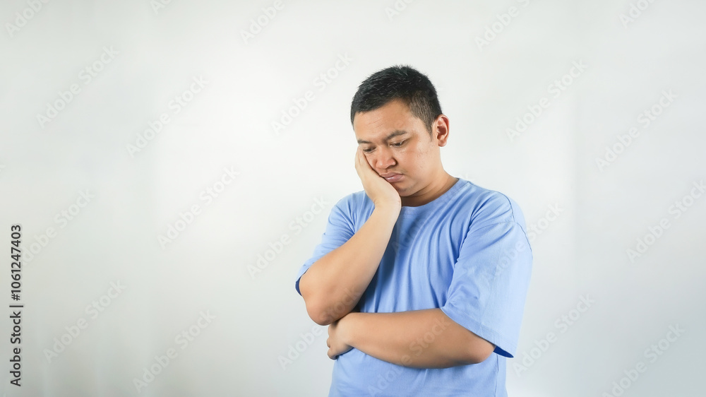 A young Indonesian man wearing a blue t-shirt with a sad face facing downwards A young Indonesian man wearing a blue t-shirt with a sad face facing downwards