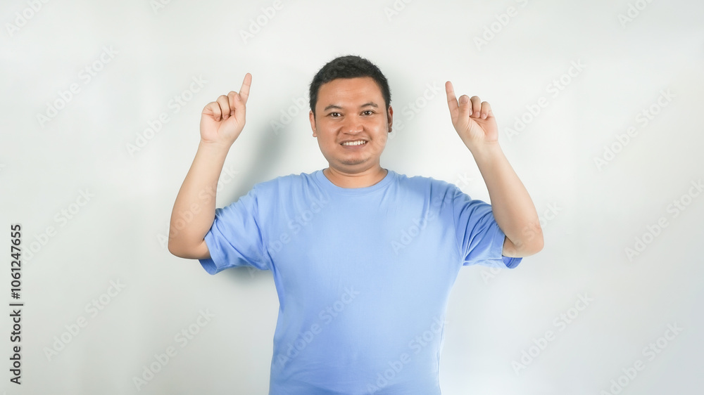 A young Indonesian man wearing a blue t-shirt with a happy face pointing upwards A young Indonesian man wearing a blue t-shirt with a happy face pointing upwards