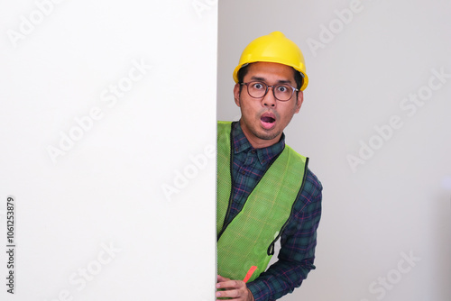 Asian civil engineer peeking from behind a wall showing shocked face expression photo