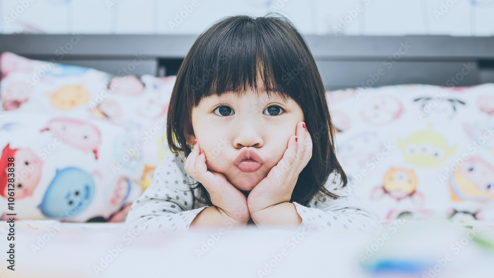 Jakarta, Indonesia - May 17, 2017 - Cute asian baby girl makes a kissing gesture on the bed. Jakarta, Indonesia - May 17, 2017 - Cute asian baby girl makes a kissing gesture on the bed.