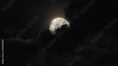 4k video of a full moon that sinks towards the bottom of the frame as clouds driven by the wind partly hide its face while they drift across from left to right.