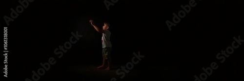 Young child standing on tiptoes flipping light switch off in a dark room, conservation, dark room, power photo