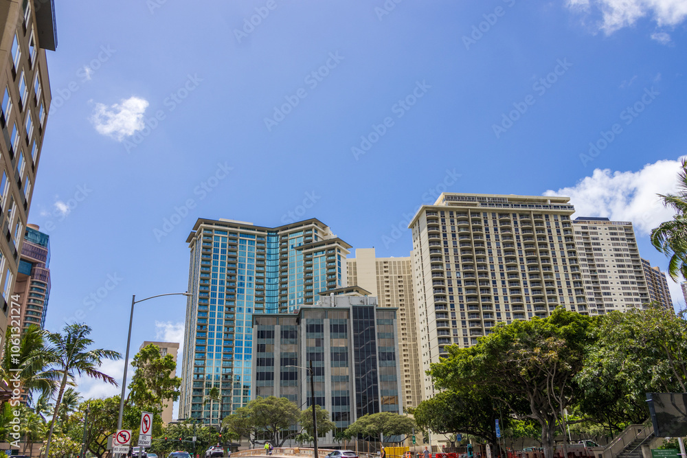 Fototapeta premium skyscrapers, apartments and office buildings with lush green trees, cars on the street, blue sky and clouds in downtown Honolulu Hawaii USA