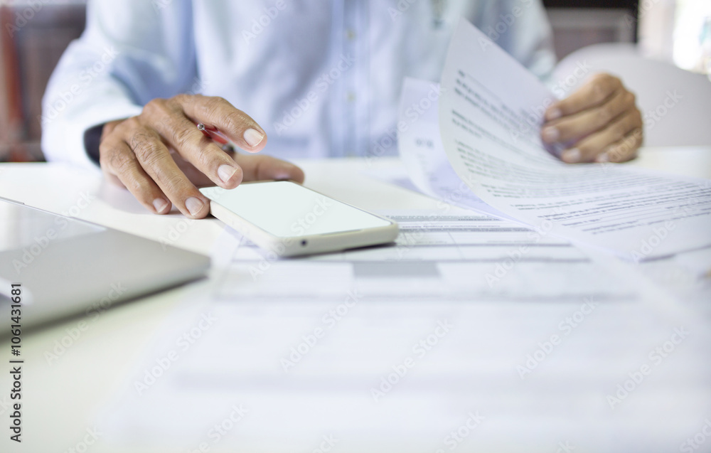 Close-up shot, asian businessman working at office using mobile phone and review document report checking business report or insurance contract before sign Close-up shot, asian businessman working at office using mobile phone and review document report checking business report or insurance contract before sign