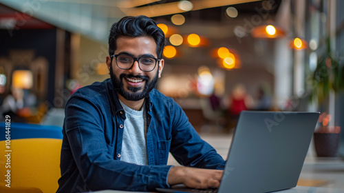 Smiling bearded Indian businessman working on a laptop in a modern office lobby. A young Indian student using a computer for remote studying, attending online webinars photo