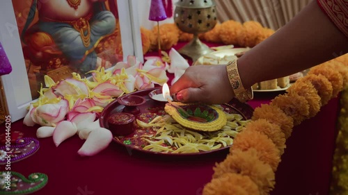 Medium close up of hands of unrecognizable woman lighting traditional Diwali lamp on decorative tray with flowers, marigold garlands, and picture of Lord Ganesha photo