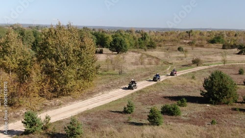 Quad bikes driving on a dirt road in the forest, sunny day, drone shot