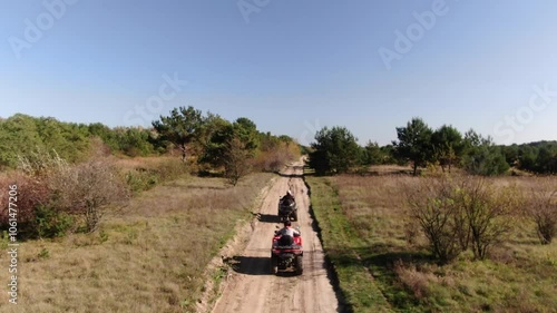 Quad bikes driving on a dirt road in the forest, sunny day, drone shot