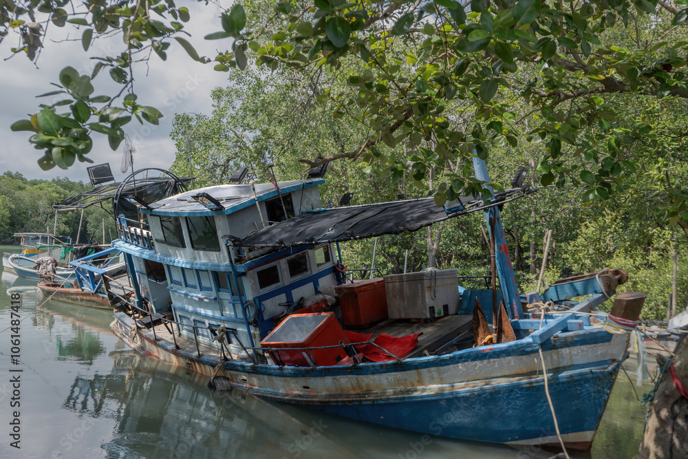 The colorful traditional wooden fishing boat is aground in the shallow water of the mangrove forest canal, Phuket, Thailand. The colorful traditional wooden fishing boat is aground in the shallow water of the mangrove forest canal, Phuket, Thailand.