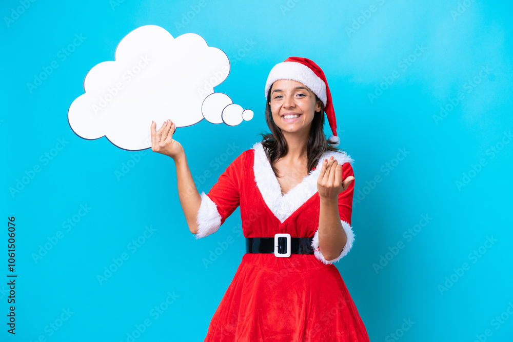 Young hispanic woman dressed as mama noel isolated on blue background holding a thinking speech bubble and doing coming gesture Young hispanic woman dressed as mama noel isolated on blue background holding a thinking speech bubble and doing coming gesture