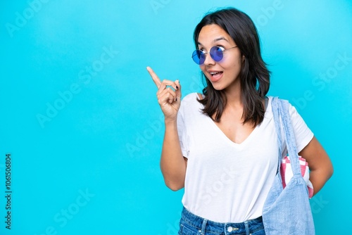 Young caucasian woman holding a beach bag isolated on blue background intending to realizes the solution while lifting a finger up