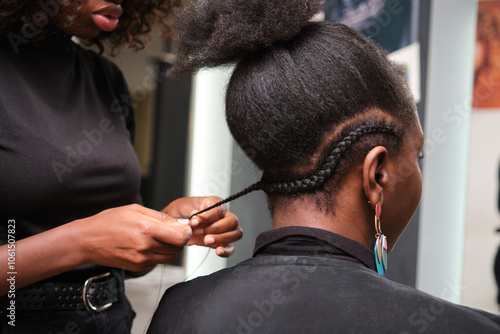 Hairdresser braiding client's afro hair in salon