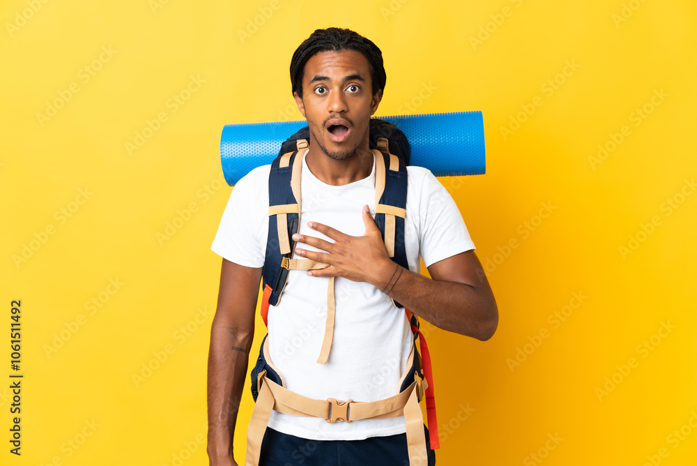 Young mountaineer man with braids with a big backpack isolated on yellow background surprised and shocked while looking right Young mountaineer man with braids with a big backpack isolated on yellow background surprised and shocked while looking right