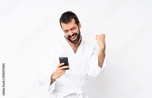 Young man doing karate over isolated white background with phone in victory position photo