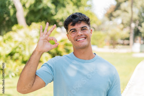 Young hispanic man at outdoors With glasses and doing OK sign photo