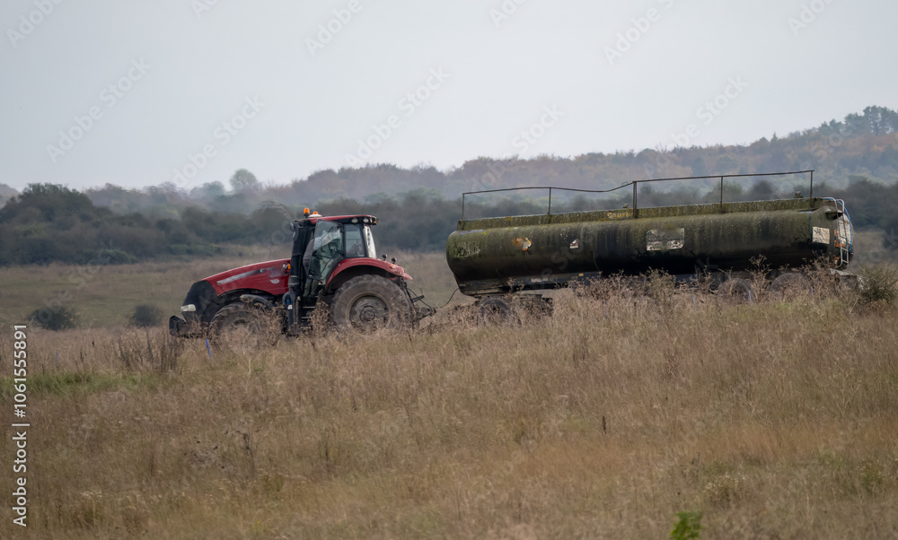 Obraz premium a large red trcator towing a 35000 water tanker in countryside