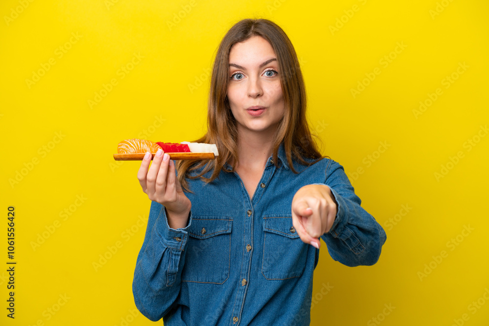 Young caucasian woman holding sashimi isolated on yellow background surprised and pointing front Young caucasian woman holding sashimi isolated on yellow background surprised and pointing front