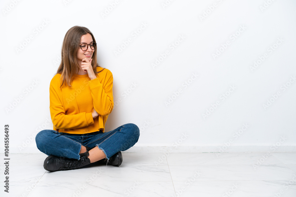 Young caucasian woman sitting on the floor isolated on white background looking to the side Young caucasian woman sitting on the floor isolated on white background looking to the side