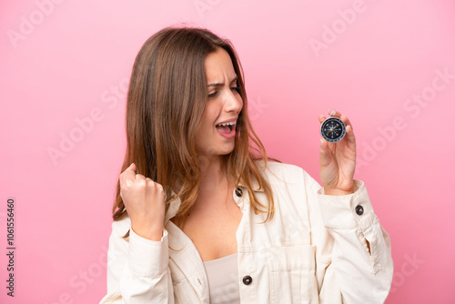 Young caucasian woman holding compass isolated on pink background celebrating a victory