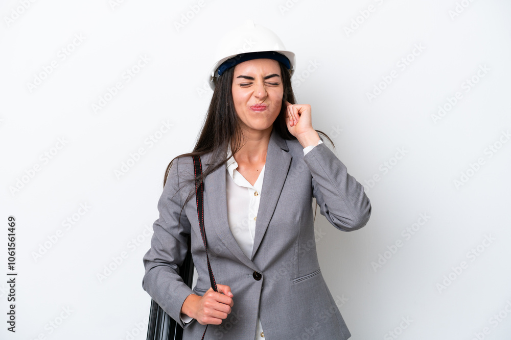 Young architect caucasian woman with helmet and holding blueprints isolated on white background frustrated and covering ears Young architect caucasian woman with helmet and holding blueprints isolated on white background frustrated and covering ears