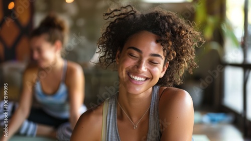 Two women enjoying a lighthearted moment in a yoga session, their radiant smiles reflecting joy and peaceful mindfulness in a calm setting.