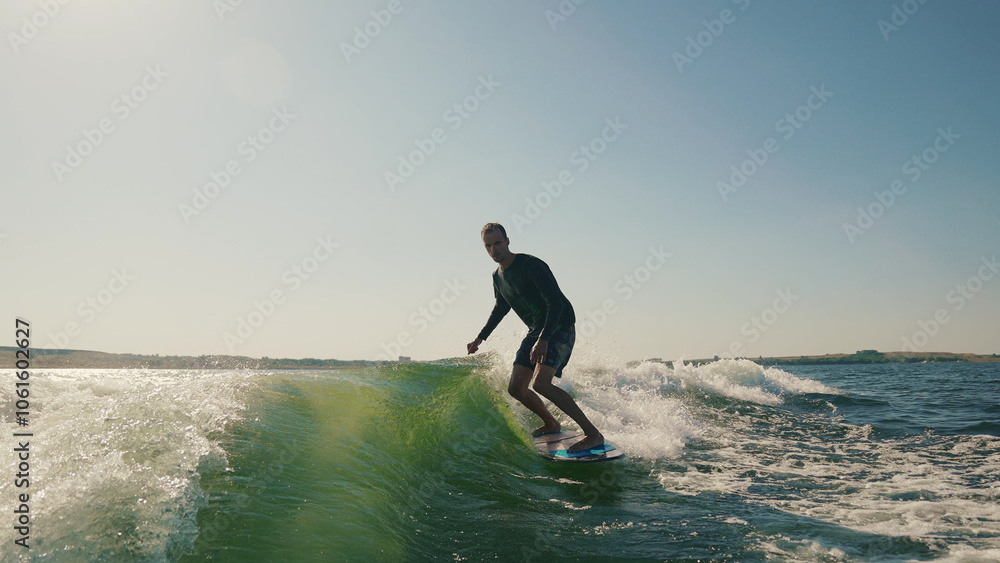 Wakeboarding behind a motor boat on the water surface. An athlete performs tricks while balancing on a board. The scene conveys the dynamics, speed and adrenaline of water extreme sports Wakeboarding behind a motor boat on the water surface. An athlete performs tricks while balancing on a board. The scene conveys the dynamics, speed and adrenaline of water extreme sports