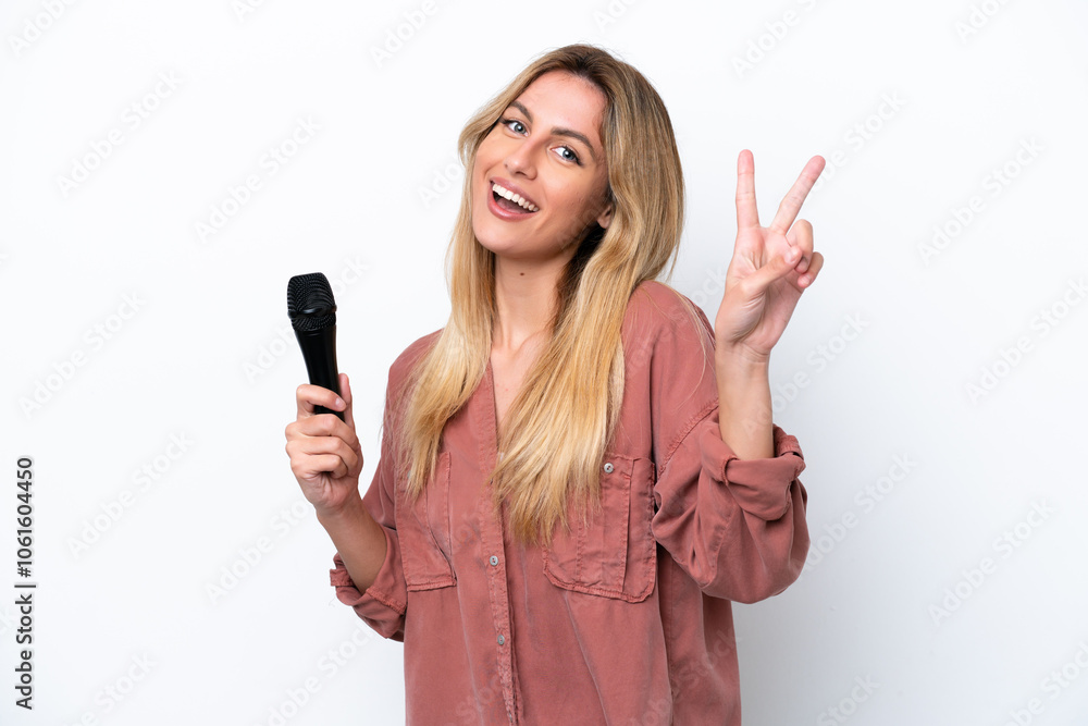 Singer Uruguayan woman picking up a microphone isolated on white background smiling and showing victory sign Singer Uruguayan woman picking up a microphone isolated on white background smiling and showing victory sign
