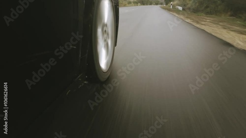 Close-up cinematic POV shot of an wet asphalt road while Car is driving on the highway right tire with droplets spray on rainy day from new asphalt road surface.Drain or drainage, car control concept