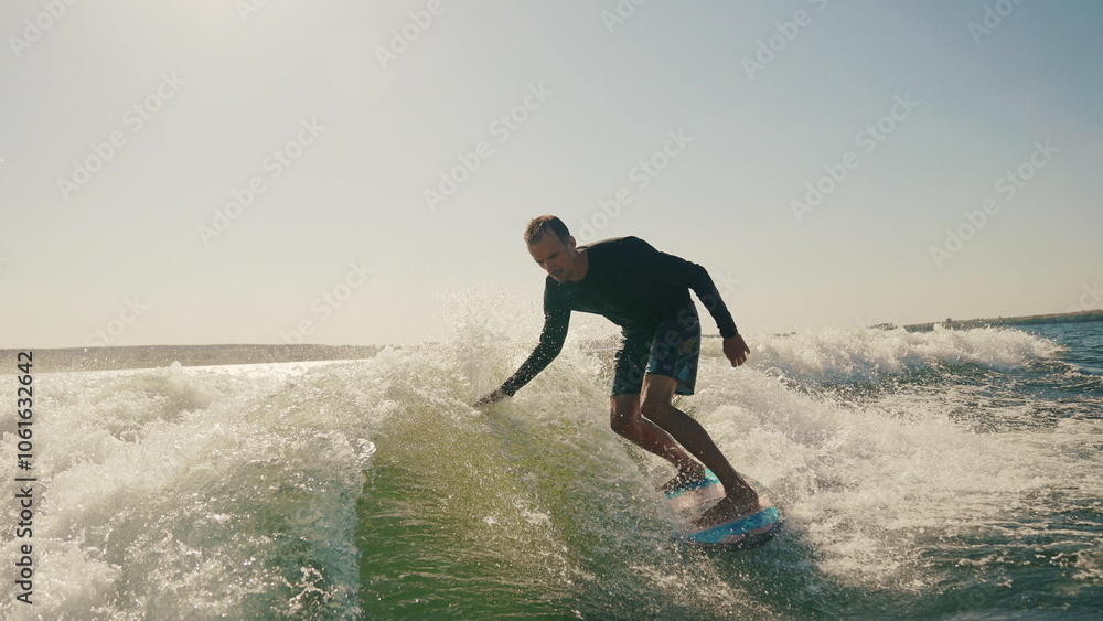 Wakeboarding behind a motor boat on the water surface. An athlete performs tricks while balancing on a board. The scene conveys the dynamics, speed and adrenaline of water extreme sports Wakeboarding behind a motor boat on the water surface. An athlete performs tricks while balancing on a board. The scene conveys the dynamics, speed and adrenaline of water extreme sports