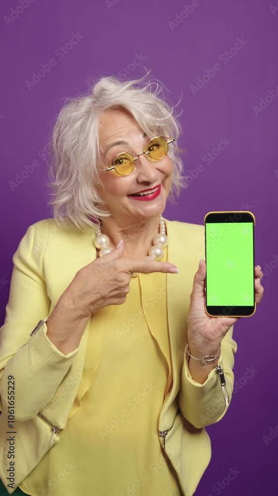 Senior influencer presenting smartphone on purple background Senior influencer presenting smartphone on purple background