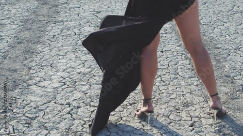 Women's legs in high-heeled shoes and fluttering black lining against the background of dry earth photo