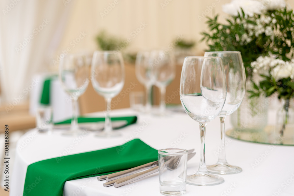 Close up of wine glasses, silver tableware and green napkins on round tables covered with white tablecloth. Close up of wine glasses, silver tableware and green napkins on round tables covered with white tablecloth.