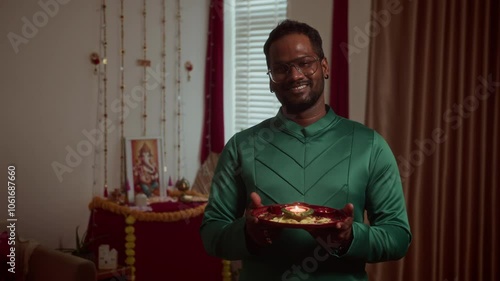 Medium portrait of cheerful Indian man in traditional outfit holding tray with burning diya and smiling at camera while celebrating Diwali photo