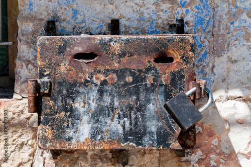 Black, rusted tzedakah box for collecting coins for charity, mounted on a stone wall in a religious neighborhood of Jerusalem, Israel. photo