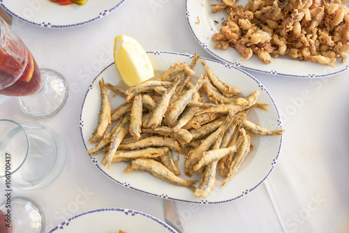 Top view of traditional Spanish fried fish dishes like whitebait or small anchovies with fresh lemon wedges, ready to share on a white tablecloth setting