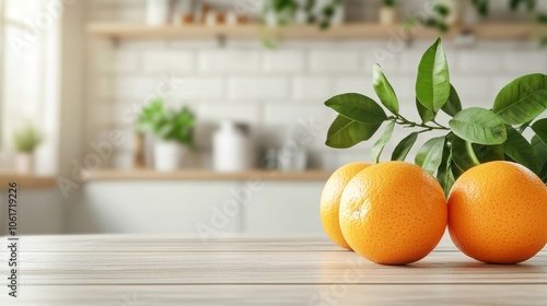 Wooden tabletop displaying fresh oranges and a green plant against a blurred kitchen setting