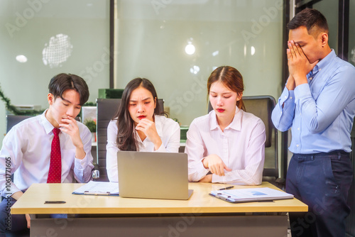 Two men and two women, including boss and employees, discuss recent mistake. Expressions of disappointment and constructive criticism create a tense, reflective atmosphere around laptops and desks.