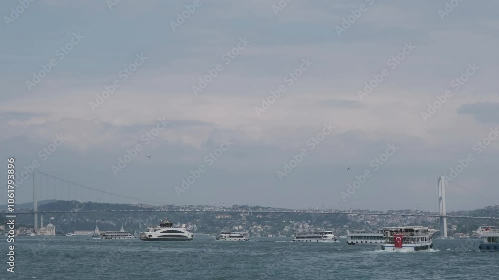 A view of the Bosphorus from a moving boat, featuring the large suspension bridge that connects Europe and Asia. Numerous tourist boats sail across the water ahead of us. A view of the Bosphorus from a moving boat, featuring the large suspension bridge that connects Europe and Asia. Numerous tourist boats sail across the water ahead of us.