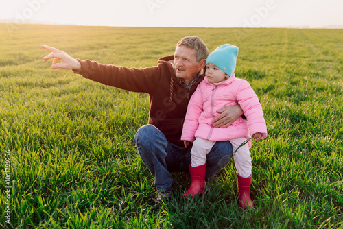 Grandfather with granddaughter in the farm field looking somewhere with sunshine