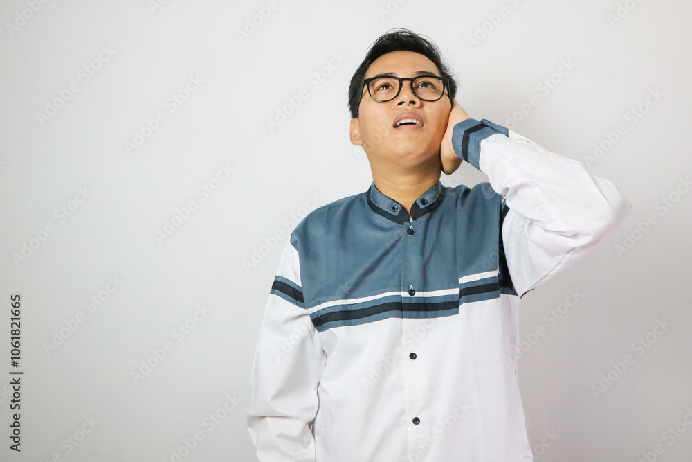 Young asian muslim man wearing moslem clothes and prayer mats in his shoulder. He is on the call to prayer or adzan Young asian muslim man wearing moslem clothes and prayer mats in his shoulder. He is on the call to prayer or adzan