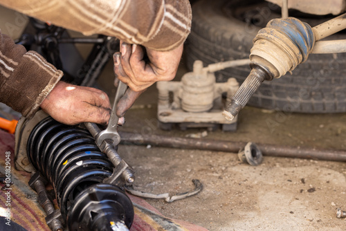 Dirty and calloused hands of experienced mechanic compressing coil spring during DIY car repairs. Closeup.