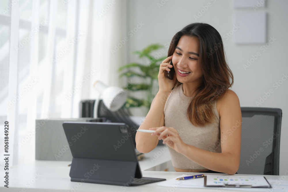 Businesswoman smiling while talking on the phone and working on a tablet in a bright modern office. Businesswoman smiling while talking on the phone and working on a tablet in a bright modern office.