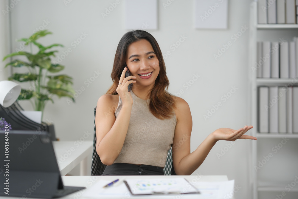 Businesswoman talking on the phone at her desk in the office, surrounded by documents and a laptop, expressing positivity and confidence. Businesswoman talking on the phone at her desk in the office, surrounded by documents and a laptop, expressing positivity and confidence.