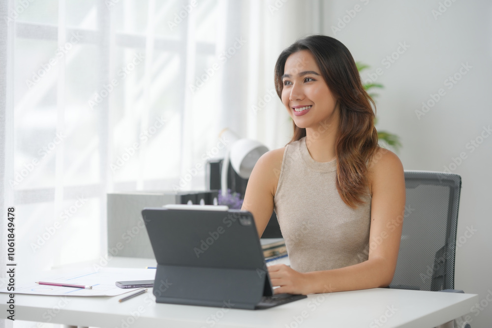 Happy professional woman working on laptop at a modern office desk, with natural light streaming through large windows, creating a bright workspace. Happy professional woman working on laptop at a modern office desk, with natural light streaming through large windows, creating a bright workspace.