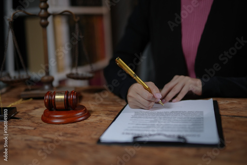 Фотография Close-up of a person signing legal documents at a desk with a gavel and scales of justice in the background, indicating a legal or judicial context