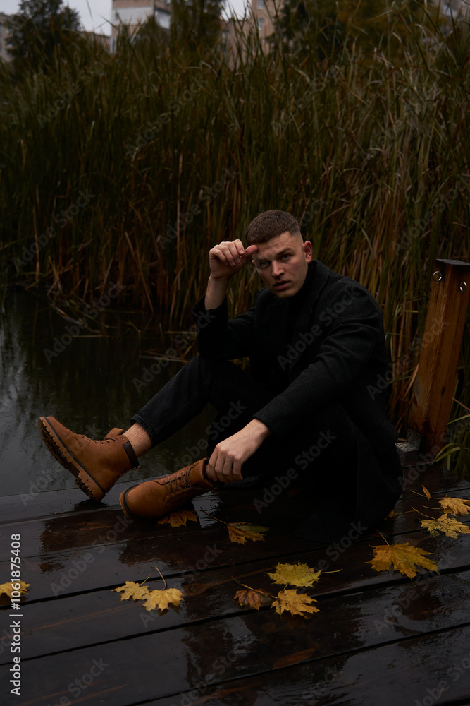A European man in a black coat walks in the park near the water at dusk in autumn A European man in a black coat walks in the park near the water at dusk in autumn