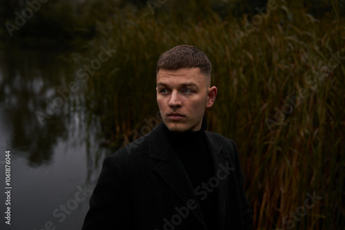 A European man in a black coat  walks in the park at dusk in autumn