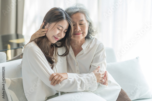 portrait of bonding senior mother and adult daughter sitting on couch and embracing together in living room,family,hugging with love, smile,affection