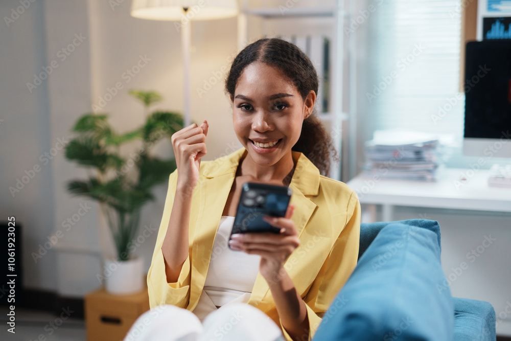 Young businesswoman feeling happy while reading good news on her smartphone and raising her fist, celebrating success Young businesswoman feeling happy while reading good news on her smartphone and raising her fist, celebrating success